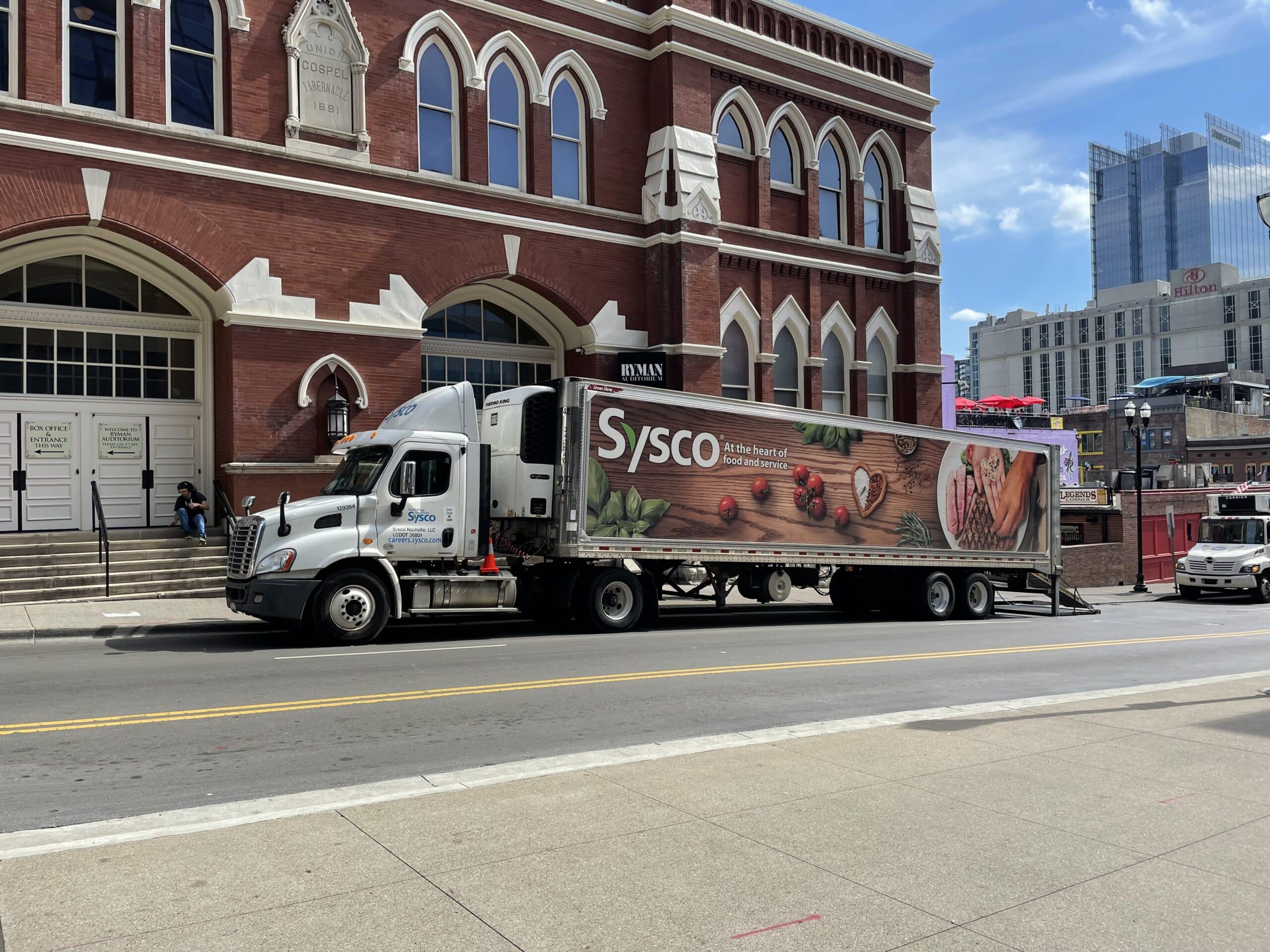 Sysco delivery truck featuring custom vehicle wrap parked in front of red brick building